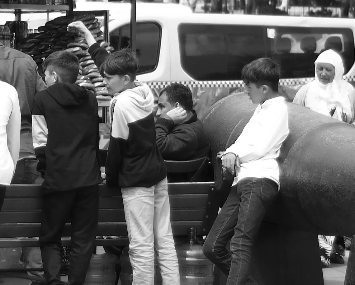 Black-and-white street scene, boys at a simit cart, a bench and a white van