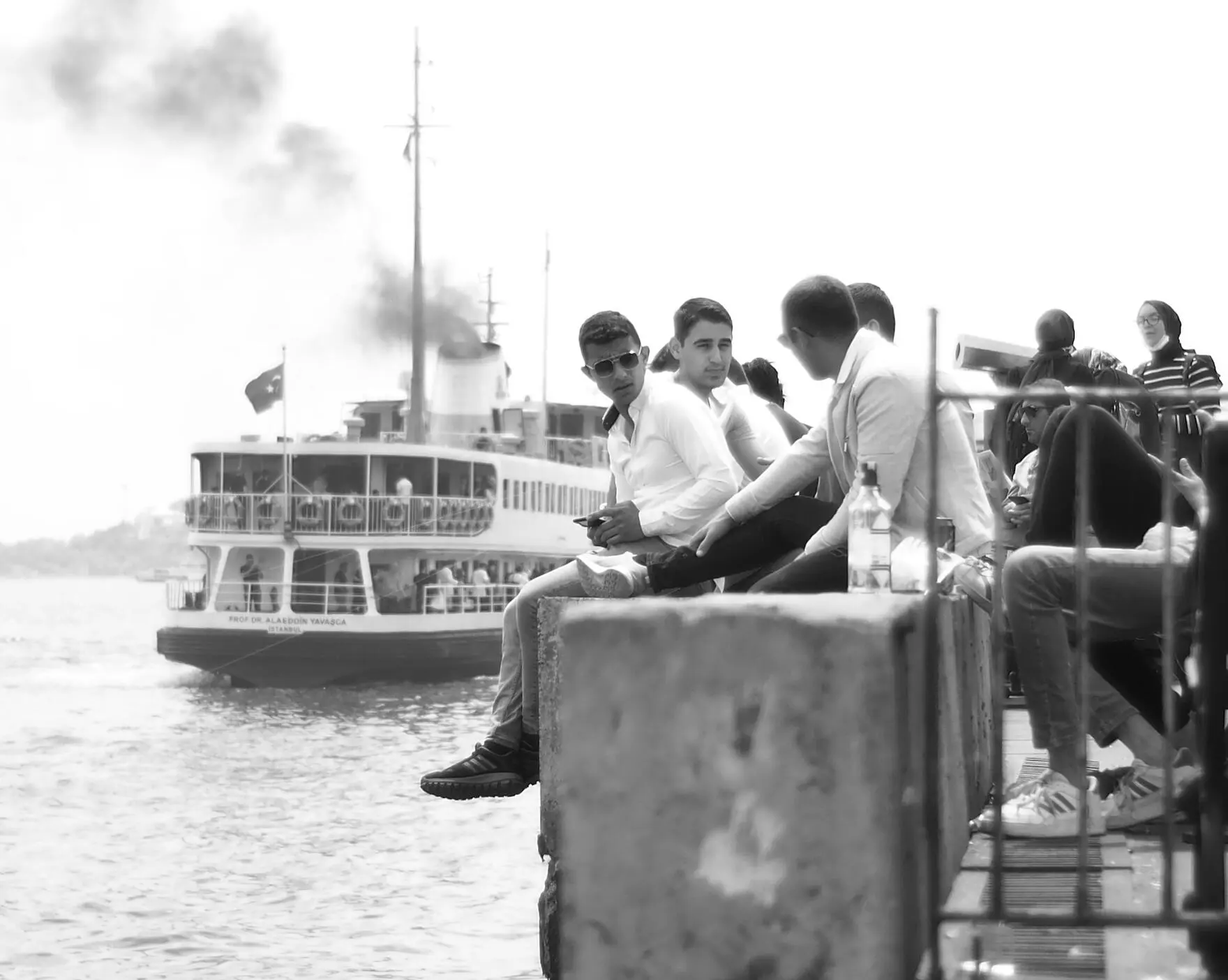 Black-and-white photo of young men on a seawall as an Istanbul ferry passes