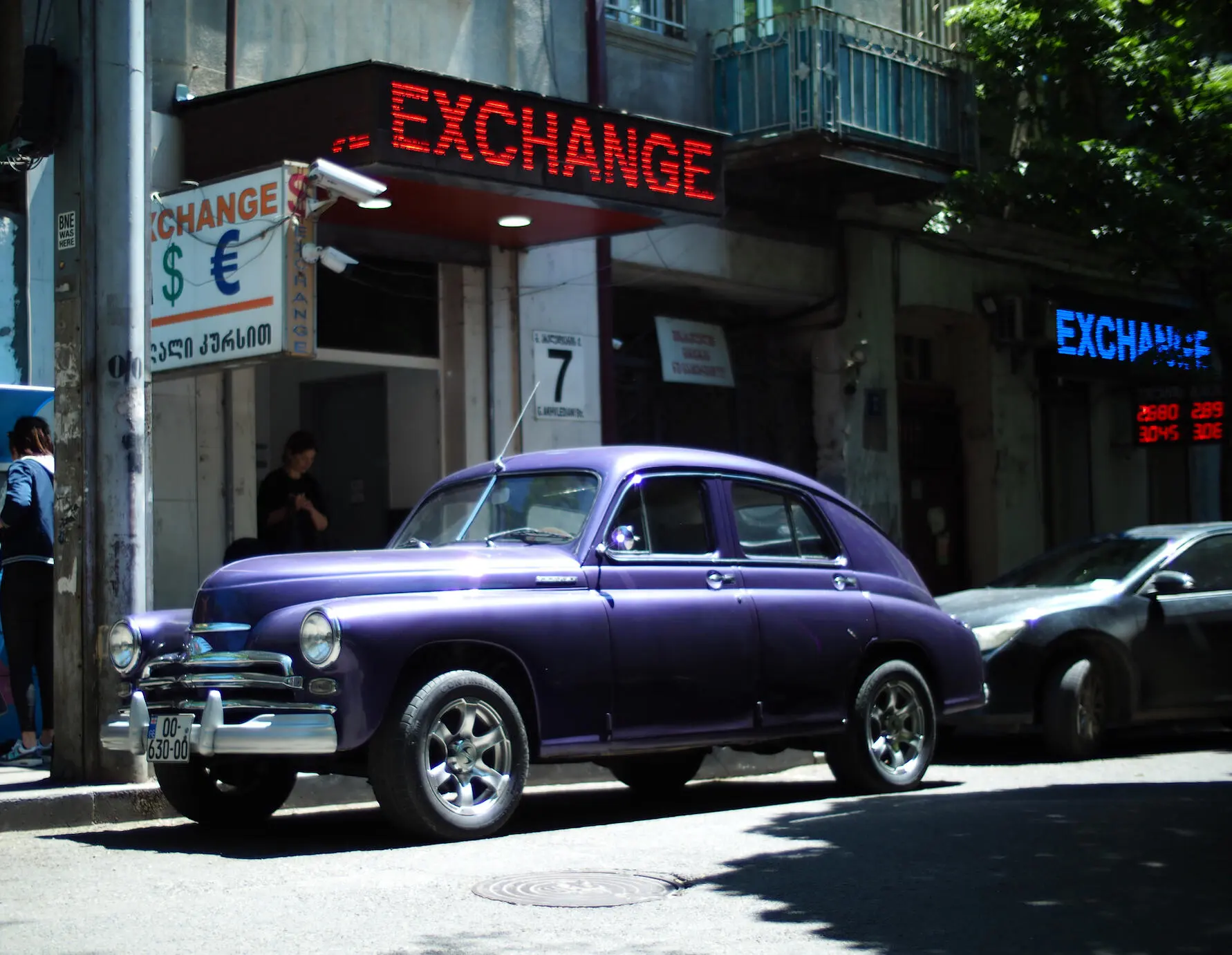 Vintage purple sedan outside currency exchange shops on a sunny street