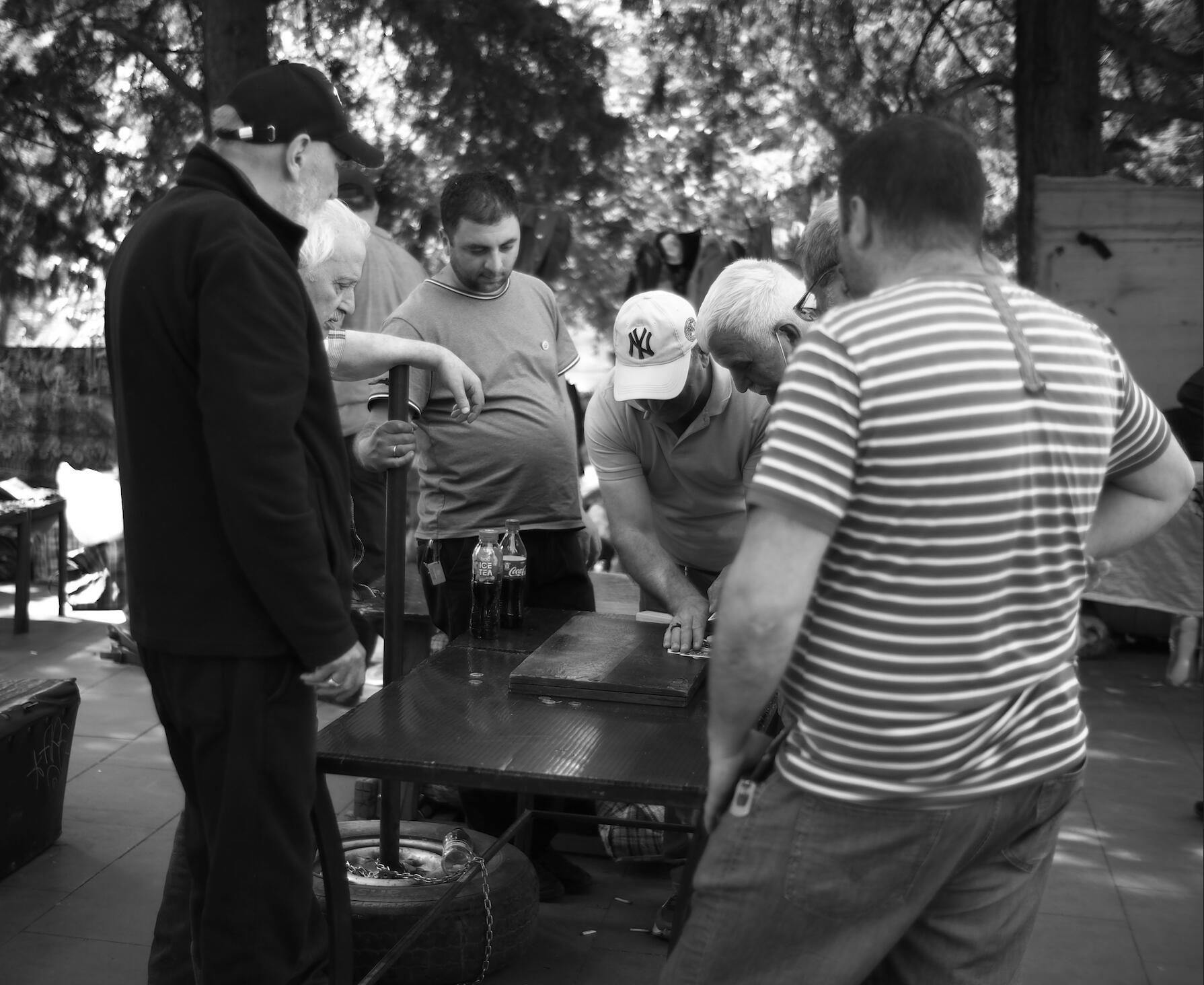 Black-and-white photo of men watching a game at an outdoor table