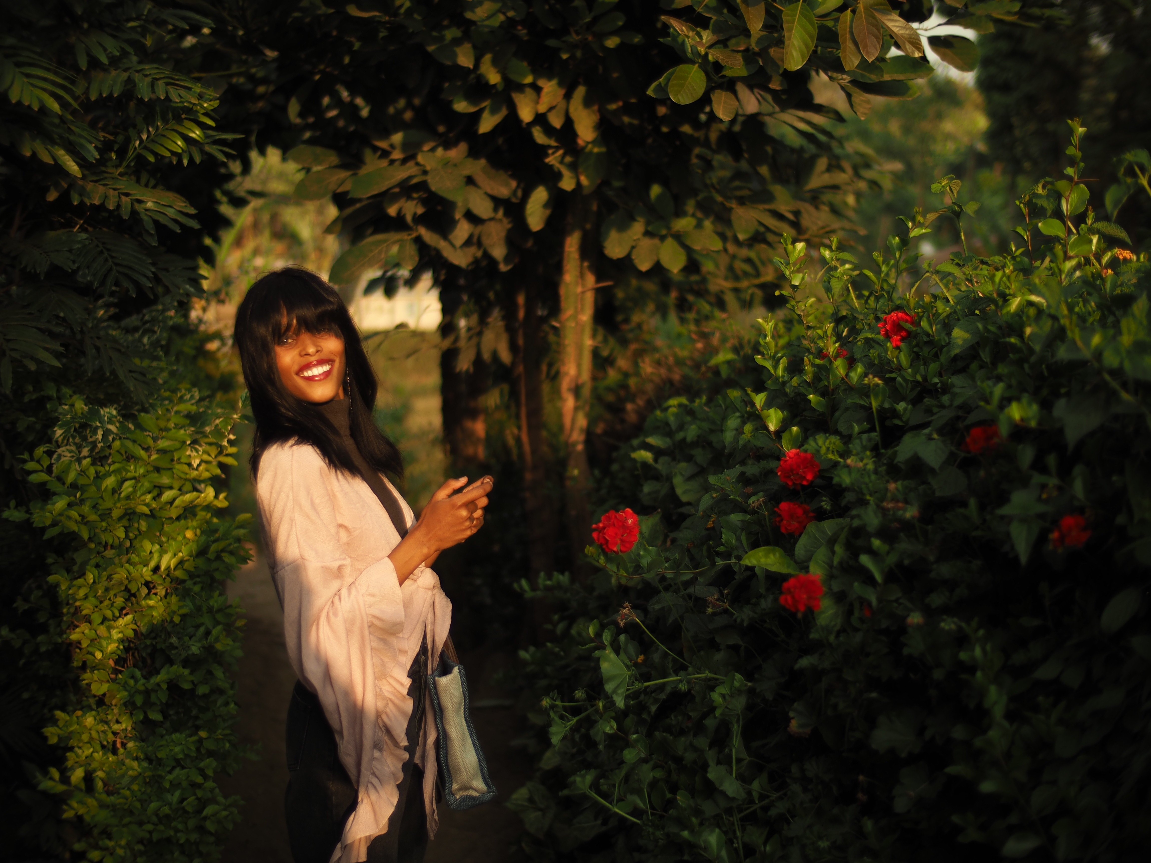 Smiling woman in a pink ruffled blouse looking back on a shaded garden path