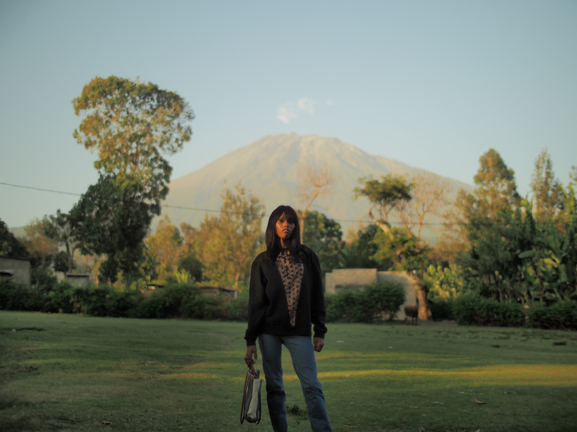 Woman in a black cardigan on a grass field in front of a big mountain