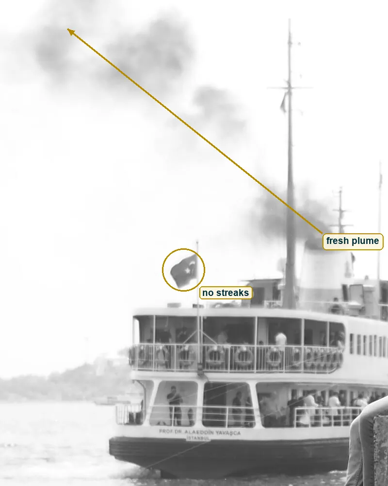 Left half of the photo with the smoke plume rising from the funnel and the flag marked
